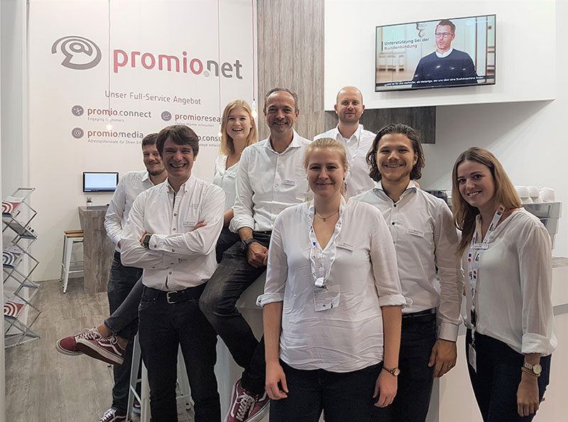 Mitarbeiter der promio.net GmbH posieren vor dem Stand auf der DMEXCO 2018